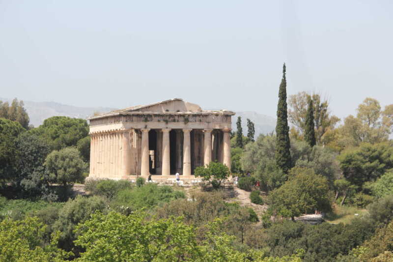 Ancient Greek temple surrounded by greenery under a clear sky.