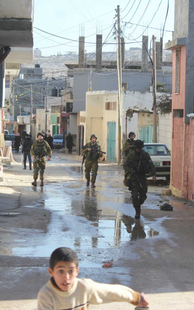 Soldiers patrol a wet urban street in a tense environment.